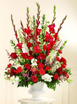 A traditional piece, this arrangement of red carnations, red roses, white Stock and or Snapdragons, larkspur with pink filler flowers in a white plastic urn is perfect for any ceremony where you need a large floral display.