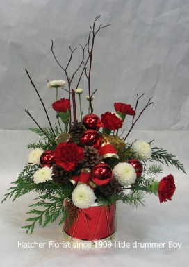 Little Drummer boy arrangement for Christmas. Keepsake, ceramic drum, pine, balls, dog wood, pine, and fir form the base for this arrangement. Pompons, red carnations and cones finish the design. We can deliver during the Holidays for you.