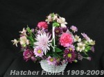 A pastel or white basket filled with long lasting, mauve, pink and purple blooms. alstroemeria, anastasia mums, carnations, and mixed mums.