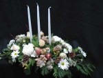 White Christmas – you can almost hear the song in the living room! A grand centrepiece with 3 white tapers, Versillia Roses, Cones, a decorative fruit cluster, Million Star Gypsophila, crisp white Chrysanthemums, and fresh fragrant Christmas greenery.