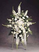 A noble tribute featuring pristine white flowers such as Carnations, Pompons, Monte Casino, Snapdragons, Stock, and elegant greens accented with a white ribbon.