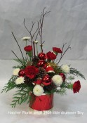 Little Drummer boy arrangement for Christmas. Keepsake, ceramic drum, pine, balls, dog wood, pine, and fir form the base for this arrangement. Pompons, red carnations and cones finish the design. We can deliver during the Holidays for you.